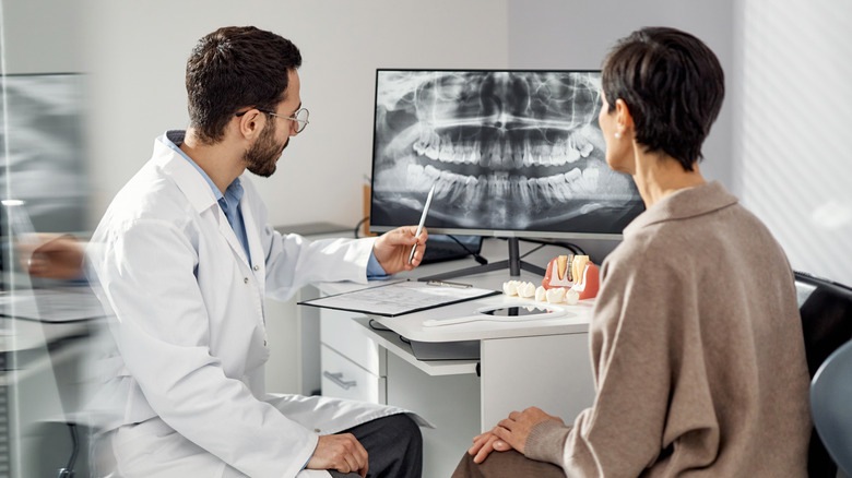 A dentist explaining the results of an oral scan shown on a monitor to a patient.