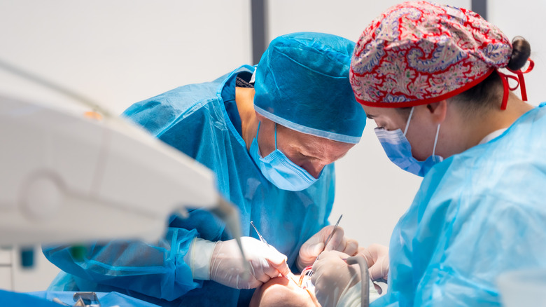 A dentist performing oral surgery while a dental technician assists