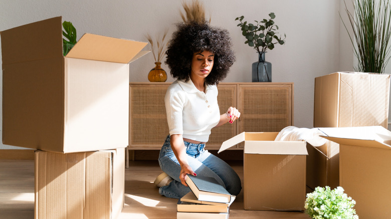 A woman kneeling on the floor taking books out of cardboard boxes