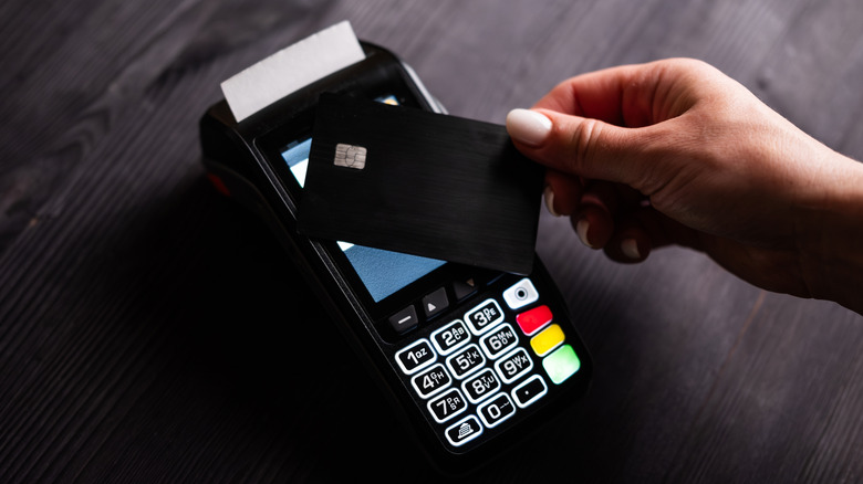 A woman holds a credit card up to a reader to use its tap-to-pay function