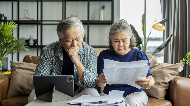 Older couple looking over paperwork while seated in living room.