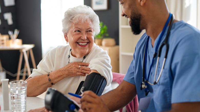 A senior woman smiling at a male nurse checking her blood pressure.