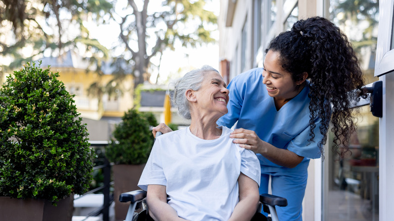 Happy home caregiver helping a senior woman in a wheelchair and smiling at her.