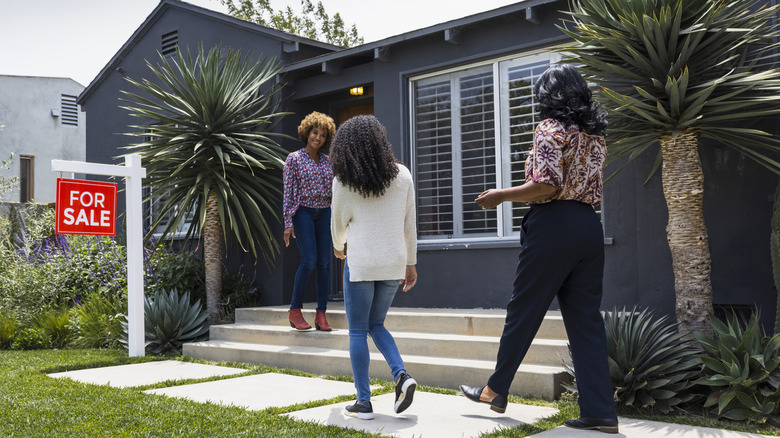 three women walking into a house with a for sale sign outside
