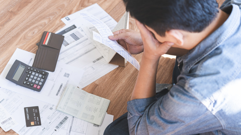 frustrated young man paying bills with a calculator and credit card
