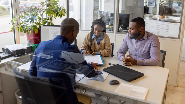 A couple signing contract papers for buying new car at dealership.