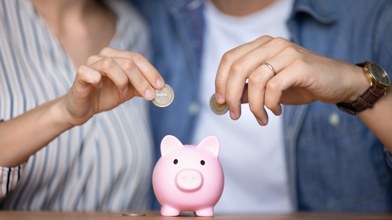 Hands of young couple throwing coins into ceramic piggy bank