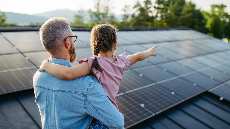Rear view of dad with girl on roof with solar panels, hugging