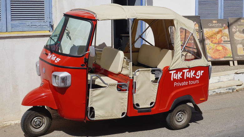 A bright red tuk-tuk used for private tours parked outside a restaurant.