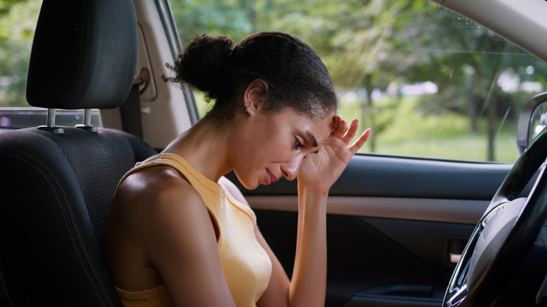 A young woman sits in her car disappointed