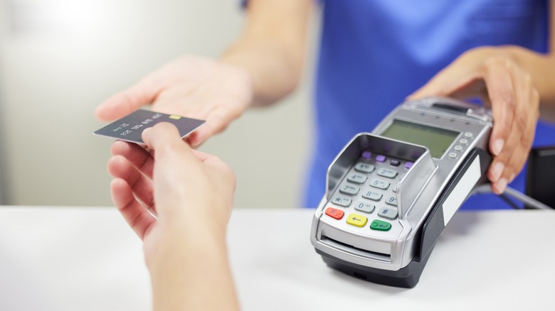 Person handing over credit card to person in blue with card reader.