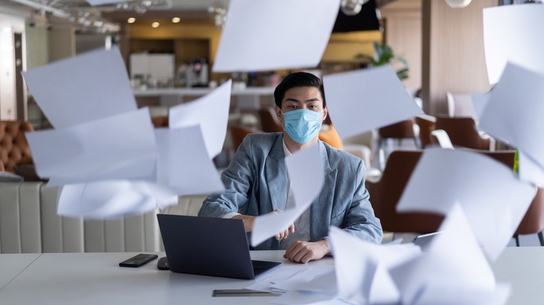 A person sitting in an office while sheets of paper blow around the room